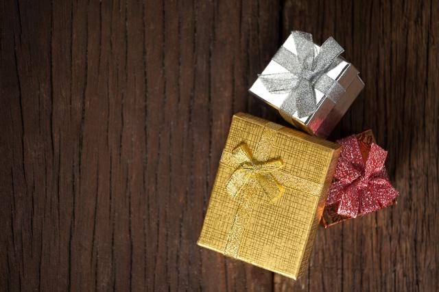 Colorful gift boxes with shiny ribbons placed on a wooden table. Ideal for holiday-themed designs, Christmas promotions, festive greeting cards, and celebration invitations.