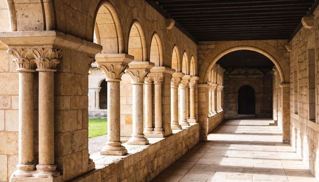 Sunlit romanesque cloister with arched colonnade, paired columns and stone walkway