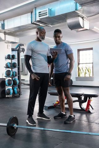 Coach reviewing tablet with client during strength training session in modern gym