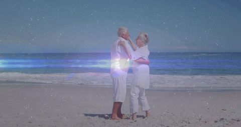 Senior couple embracing on sandy beach with dreamy light flare and nostalgic grain texture