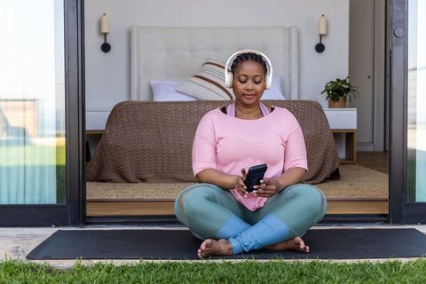African american woman meditating on yoga mat at sliding door wearing headphones