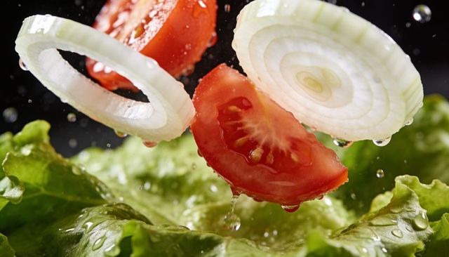 Floating tomato slices and onion rings dripping over fresh lettuce, close-up splash