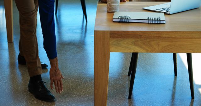 Person stretches beside a wooden desk with a laptop and notebook, illustrating work-life balance. Ideal for health, wellness, ergonomics, and office productivity marketing. Suitable for blogs, articles, or promotions related to workplace wellness, employee health, and office design.