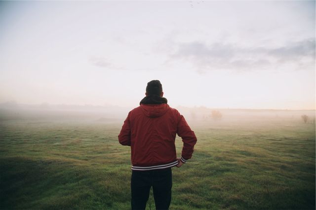 Picture captures man standing in foggy meadow enjoying peaceful morning. Great for themes related to nature, relaxation, and finding peace in solitude. Perfect for use in blogs about wellness, meditation, nature retreats, or personal reflection.