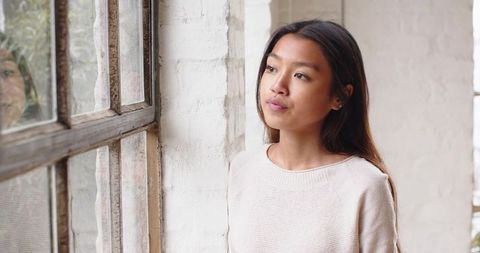 Contemplative Asian Woman Standing by Window in Serene Interior