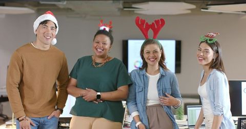 Diverse coworkers smiling and celebrating holiday in modern office with festive headwear