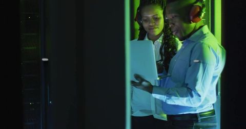 IT professionals collaborating using laptop in data center aisle with green lighting