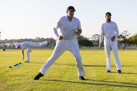 Cricket players practicing fielding drills on grass during golden hour training session