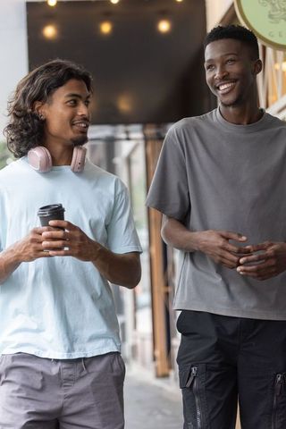 African american friends walking and laughing outside cafe holding coffee and headphones