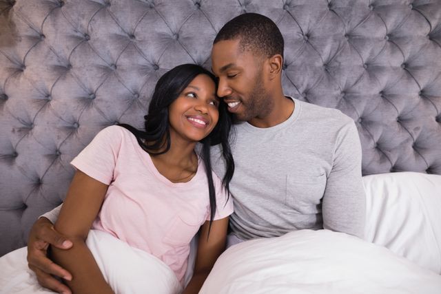 Smiling couple embracing while sitting on bed - Download Free Stock Photos Pikwizard.com