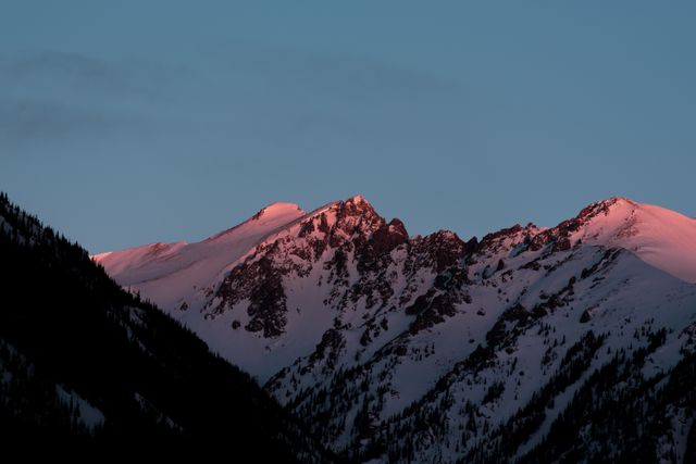 Image depicts majestic snowy mountain peaks illuminated by a pink sunrise, creating a tranquil and scenic winter landscape. Ideal for promoting adventure tourism, winter sports destinations, nature conservation, and inspirational content. Can be used in travel brochures, websites, social media posts, and outdoor activity promotions.