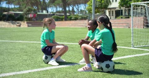 Youth girls sitting on soccer balls chatting on turf during team practice and bonding
