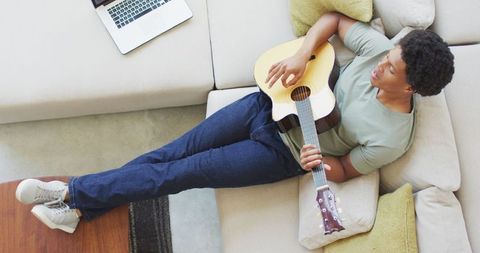 Man Relaxing on Sofa Playing Guitar During Leisure