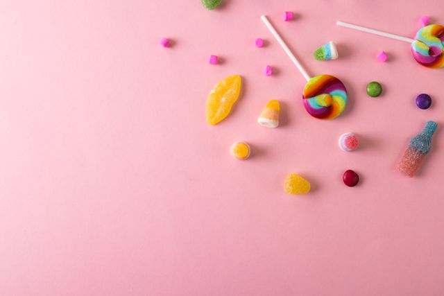 Overhead view of scattered lollipops with candies by copy space against pink background. unaltered, unhealthy eating and sweet food concept.