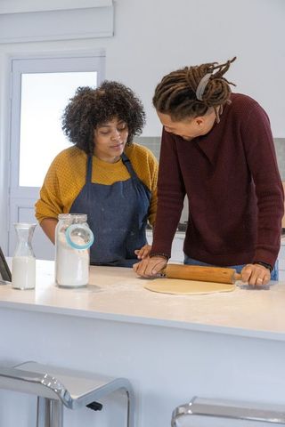 African american couple rolling dough at kitchen island baking together in modern sunlit kitchen