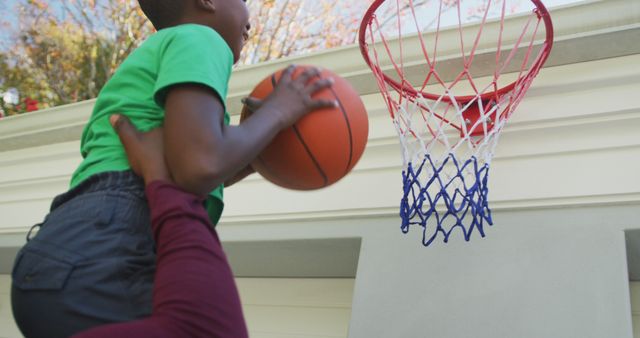 African american dad carrying his son to make a dunk in the basketball hoop - Download Free Stock Photos Pikwizard.com
