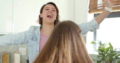 Friends laughing and celebrating morning in sunlit kitchen with casual denim jacket