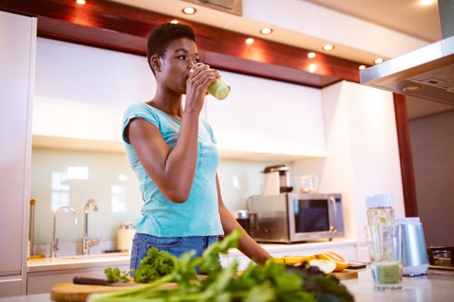 African american woman drinking fresh smoothie in kitchen. domestic lifestyle and self care, enjoying leisure time at home.