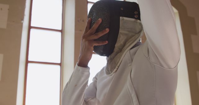 Fencing Athlete Adjusting Helmet in Sunlit Room - Download Free Stock Images Pikwizard.com