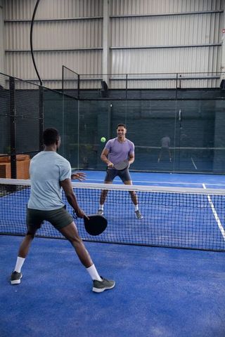 Competitive padel rally on indoor blue court with diverse male players holding paddles