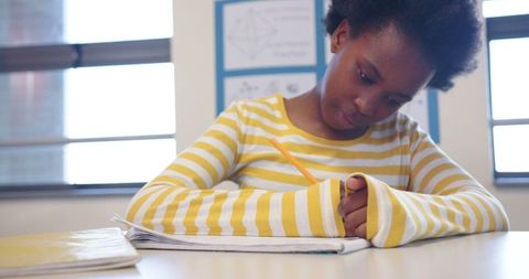 Young Girl Focused on Writing in Classroom Setting Near Window