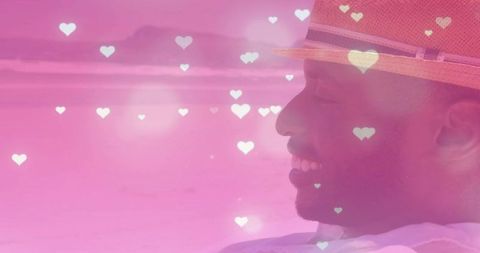 Smiling man reclining at pink beach wearing straw hat with dreamy heart bokeh overlay seascape