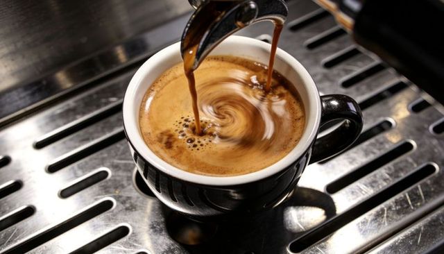 Dual-spout espresso pour creating creamy crema swirl in black cup on metal drip tray