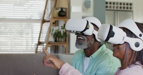Senior Couple Exploring Virtual Reality Together Wearing VR Headsets on Living Room Couch