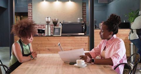 African american small business meeting in cafe reviewing documents and laptop over coffee