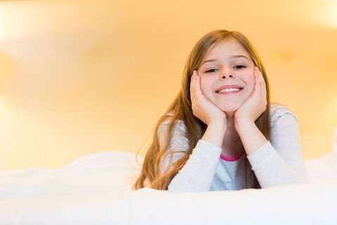 Young Girl Relaxing on White Bed with Bright Smile