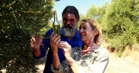Smiling Couple in Olive Orchard Holding Fresh Olive Oil Bottle - Download Free Stock Images Pikwizard.com
