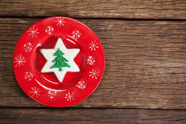 Star-shaped Christmas cookie with green tree icing on red plate with snowflake design. Ideal for holiday-themed promotions, festive greeting cards, seasonal recipes, and Christmas party invitations.