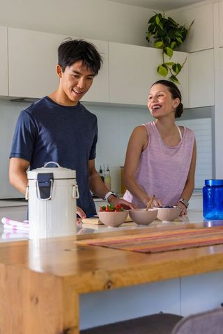 Couple preparing healthy fruit bowls at modern kitchen island, smiling and chatting
