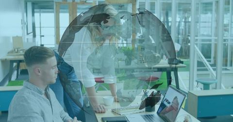 Colleagues Collaborating Over Laptop with Globe Overlay in Modern Open Office Workspace