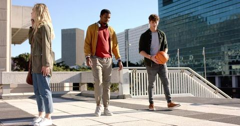 Diverse young adults walking on urban rooftop terrace holding basketball and phone