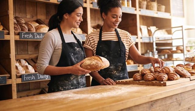 Two bakers arranging croissant tray and holding sourdough loaf on rustic wooden counter