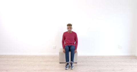 Young Man in Minimalist Room Sitting on Stool Contemplating