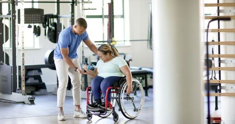 Trainer Assisting Woman with Disability Using Dumbbells in Gym