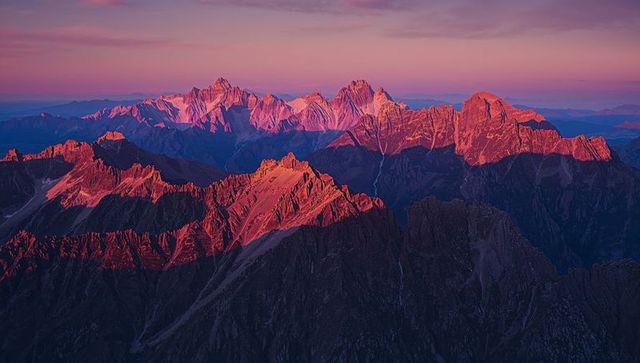 Jagged mountain peaks in red sunlight beneath pink sky