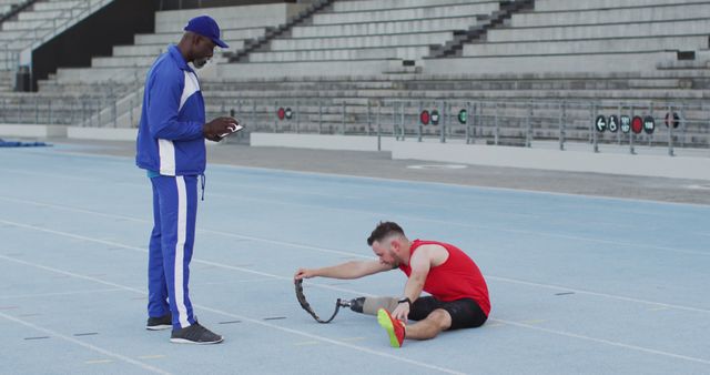 Diverse male coach and disabled athlete with prosthetic leg training and stretching. professional runner training at sports stadium.