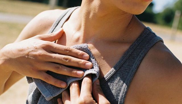 Athlete wiping sweat from chest with towel during sunny outdoor workout, closeup