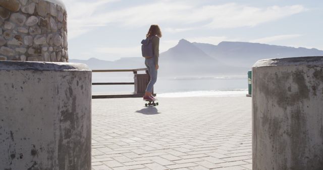Rear view of biracial woman skateboarding on sunny promenade by the sea - Download Free Stock Photos Pikwizard.com