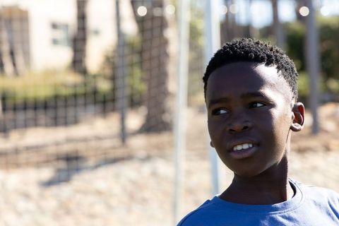 African american teen standing by soccer goal in sunlit park wearing blue t-shirt