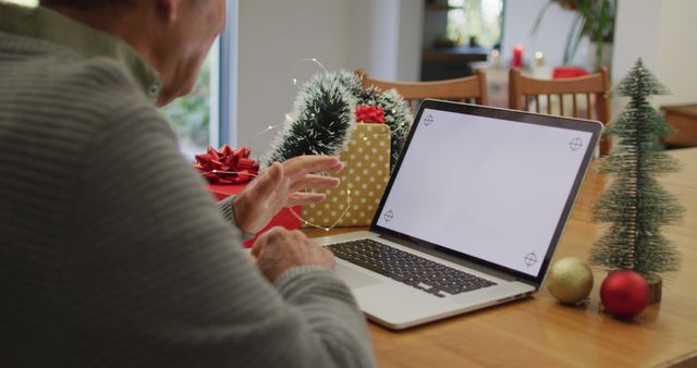 Caucasian senior man sitting at table making image call at home on laptop with copy space on screen. christmas, communication technology and celebration.