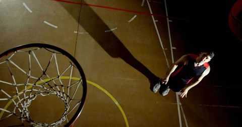 Basketball player looking up at hoop under dramatic spotlight casting long shadow