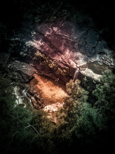 Person seen from above in remote rocky clearing within dense forest. Can be used for themes related to adventure, solitude, discovering nature, or wilderness exploration.