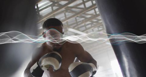 Shirtless male boxer training, throwing powerful punches on heavy bag in warehouse gym