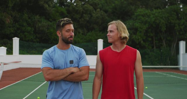 This image depicts two male friends standing on a tennis court, smiling at each other after a game. It conveys concepts like friendship, casual sports, and relaxation. Useful for content about leisure activities, sportsmanship, social interaction, and healthy lifestyles.