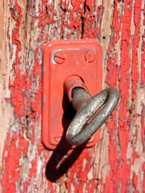 Vintage metal key inserted in a rustic red door. Exhibiting signs of age with weathered paint and worn metal. Ideal for themes of nostalgia, security, history, antique collections, and rustic decor inspiration.