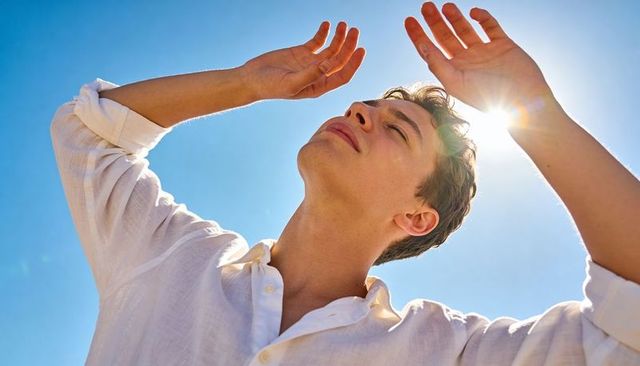 Young man shielding eyes from bright sun with hands, enjoying warm summer sunlight